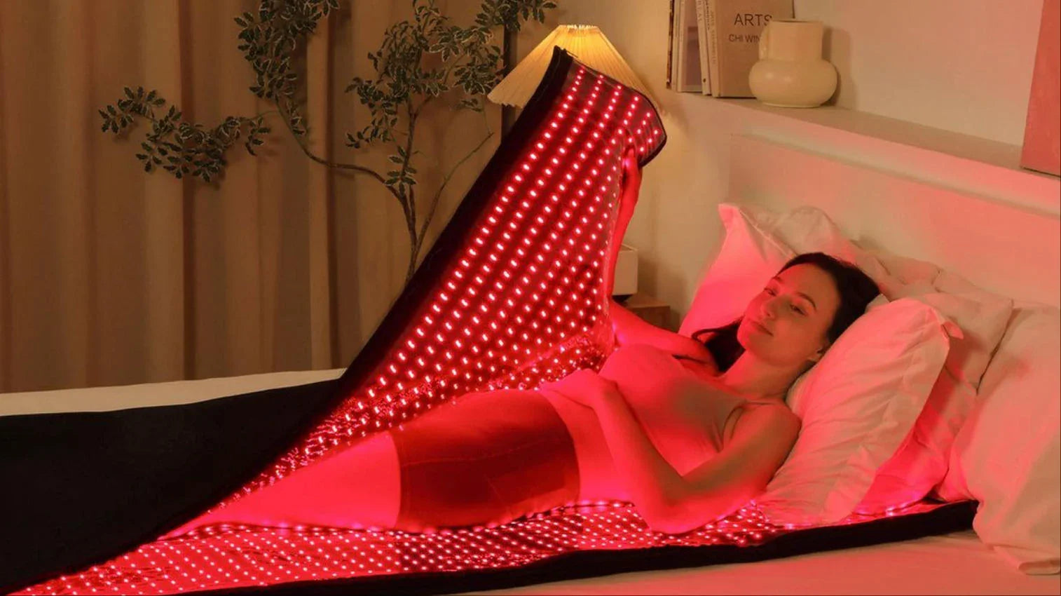 Woman relaxing under red LED light therapy blanket for at-home skin rejuvenation and pain relief